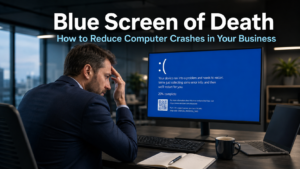 Business professional looking concerned at a computer monitor displaying a blue screen error in a modern office, representing the disruption caused by the Blue Screen of Death in business environments